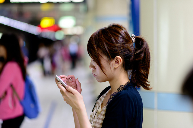 Decorative: an individual woman interacting with her cell phone in a public space.
